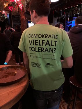 Eine Person trägt ein T-Shirt, der Rückenaufdruck sagt: Demokratie, Vielfalt, Toleranz.