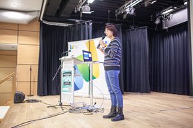 Eine Frau steht auf der Bühne und hält ein Mikrofon in der Hand