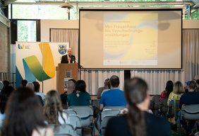 Landrat Udo Recktenwald steht auf der Bühne, vor ihm sitzende Besucher der Verasntaltung.
