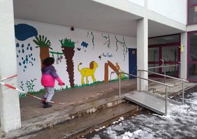 Die bemalte Wand auf dem Schulhof, an der eine Schülerin vorbeigeht.