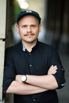 Der Referent Tobias Ginsburg steht mit verschränkten Armen an eine Mauer gelehnt.