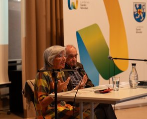 Das Ehepaar Michalski sitzt an einem Tisch auf der Bühne. Frau Michalski spricht