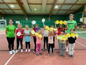 Auf einem Tennisplatz halten Kinder gelbe Papierkreise in die Luft.