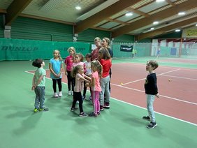Kinder und Erwachsene stehen in einer Tennishalle.