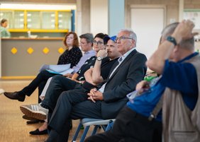 Der Referent Tobias Ginsburg sitzt neben Landrat Udo Recktenwald, zu sehen sind auch weitere Gäste der Veranstaltung.