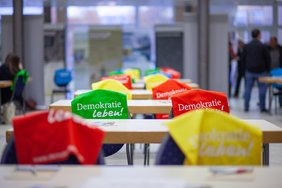 Stühle stehen an Tischen, auf die Stuhllehnen wurden bunte Taschen gelegt.