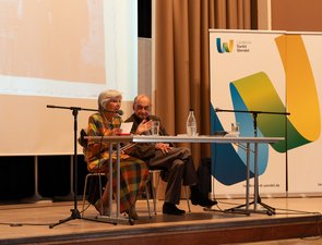 Das Ehepaar Michalski am Tisch auf der Bühne, Frau Michalski spricht und hält einen Zettel in der Hand.