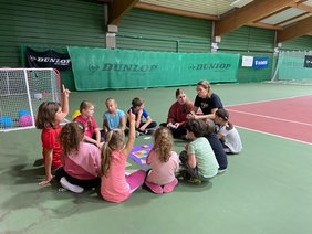 Kinder sitzen in einer Sporthalle im Kreis.