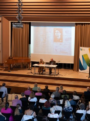 DAs Ehepaar Michalski am Tisch auf der Bühne, Teile des Publikums davor.