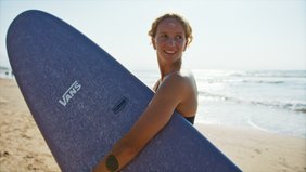 Frau mit Surfbrett unter dem Arm an einem Strand.