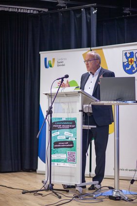 Landrat Udo Recktenwald steht an einem Rednerpult auf der Bühne.