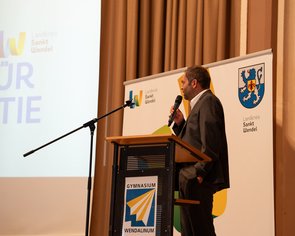 Der Schulleiter steht am Rednerpult und spricht ins Mikrofon