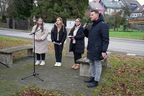 Eine Schulklasse am Ort gegen das Vergessen in Sötern, der Lehrer spricht in ein Mikrofon.