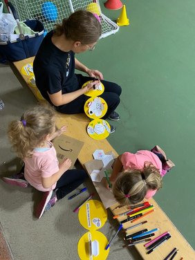 Zwei Kinder und eine erwachsene Person bemalen gelbe Papierkreise.